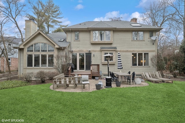 back of property with a shingled roof, a patio area, a lawn, and a chimney