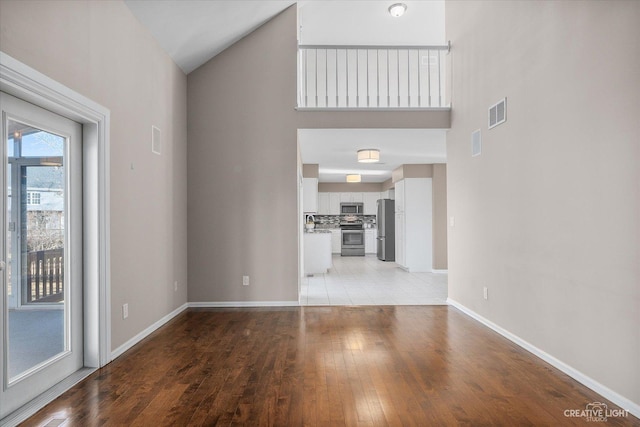 unfurnished living room featuring a high ceiling, baseboards, visible vents, and light wood finished floors