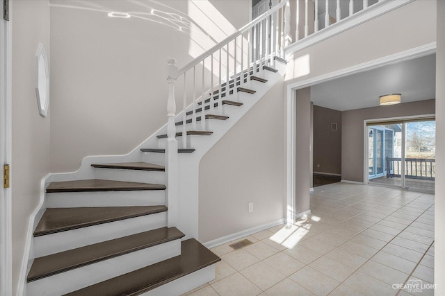 stairs with tile patterned flooring, a high ceiling, baseboards, and visible vents