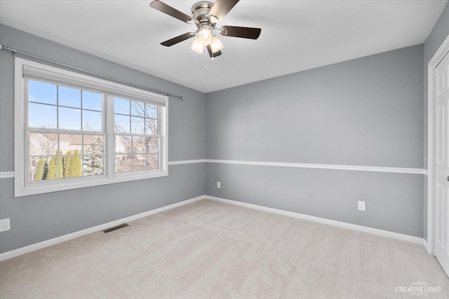 carpeted spare room with visible vents, a ceiling fan, and baseboards