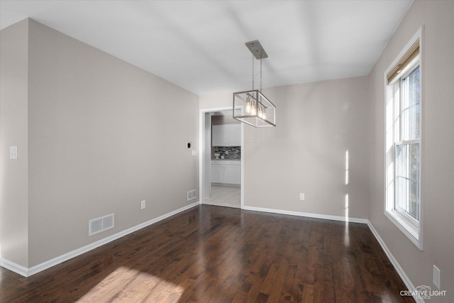 unfurnished dining area with a notable chandelier, visible vents, baseboards, and wood finished floors