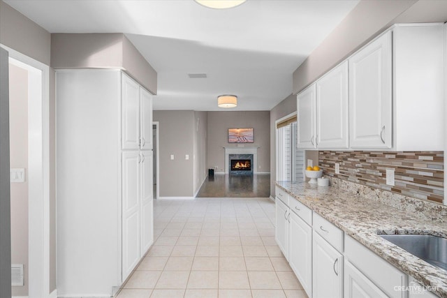 kitchen with a premium fireplace, light tile patterned flooring, decorative backsplash, white cabinetry, and open floor plan