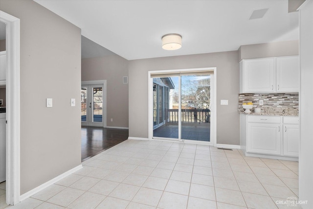 unfurnished dining area with light tile patterned floors, french doors, and baseboards