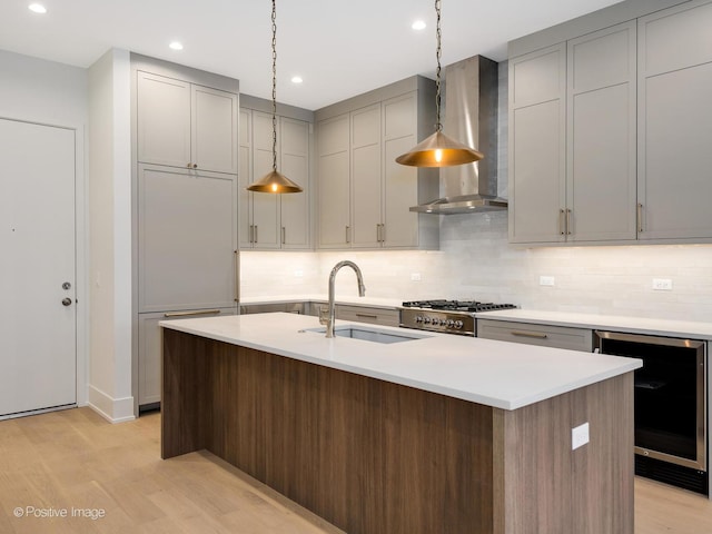 kitchen featuring sink, beverage cooler, an island with sink, and wall chimney exhaust hood