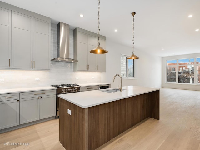 kitchen featuring light hardwood / wood-style flooring, sink, range with gas stovetop, wall chimney exhaust hood, and an island with sink