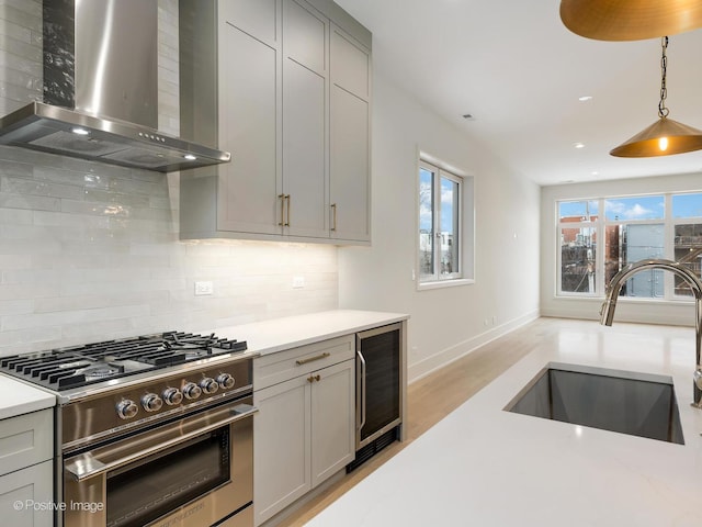 kitchen with gray cabinetry, stainless steel gas range oven, wall chimney range hood, beverage cooler, and sink