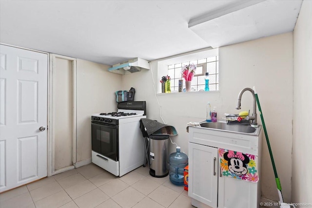 kitchen with light tile patterned floors, white gas stove, under cabinet range hood, white cabinetry, and a sink