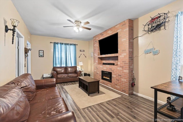 living area with ceiling fan, a fireplace, baseboards, and dark wood finished floors