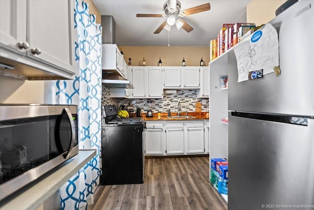 kitchen with decorative backsplash, white cabinets, appliances with stainless steel finishes, dark wood-type flooring, and a sink