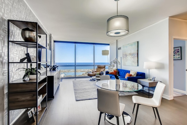 dining area featuring a water view, ornamental molding, wood finished floors, a wall of windows, and baseboards