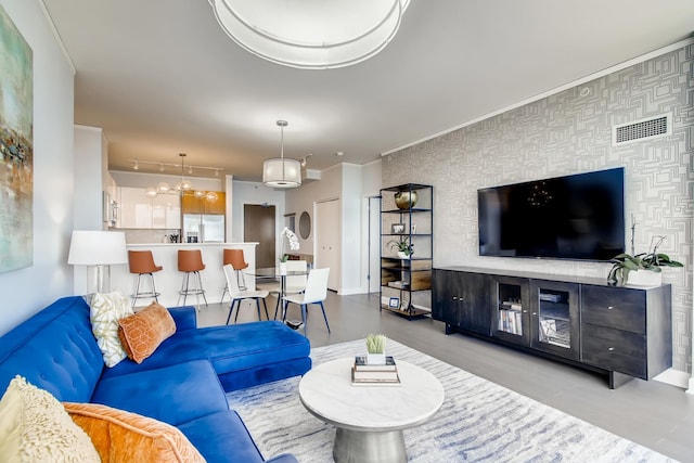 living room featuring wallpapered walls, baseboards, visible vents, an accent wall, and ornamental molding