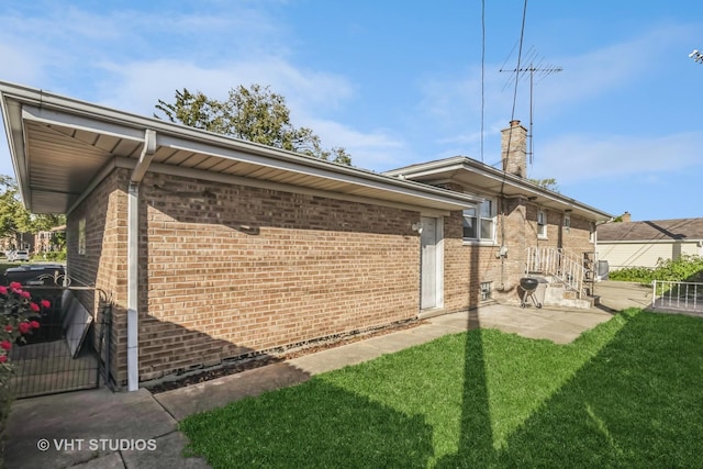 view of property exterior with brick siding, a yard, a chimney, and a patio