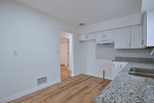 kitchen featuring sink, light stone counters, light hardwood / wood-style floors, white cabinets, and decorative backsplash