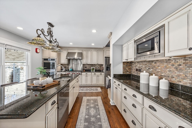 kitchen featuring a sink, appliances with stainless steel finishes, dark wood-style floors, wall chimney exhaust hood, and decorative light fixtures