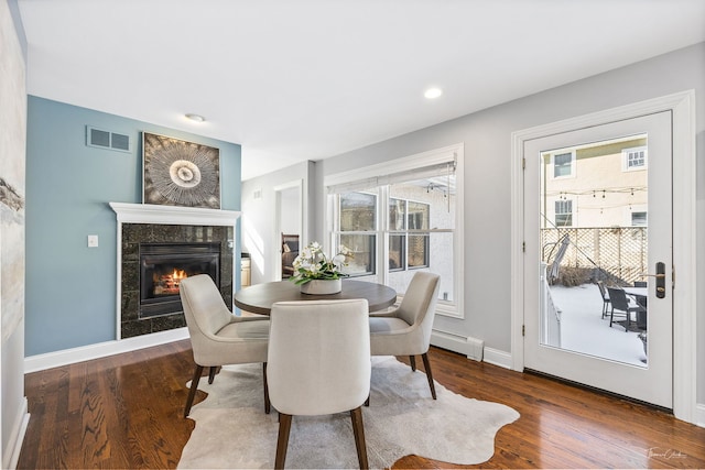 dining space with a baseboard heating unit, a fireplace, dark wood-style floors, and visible vents