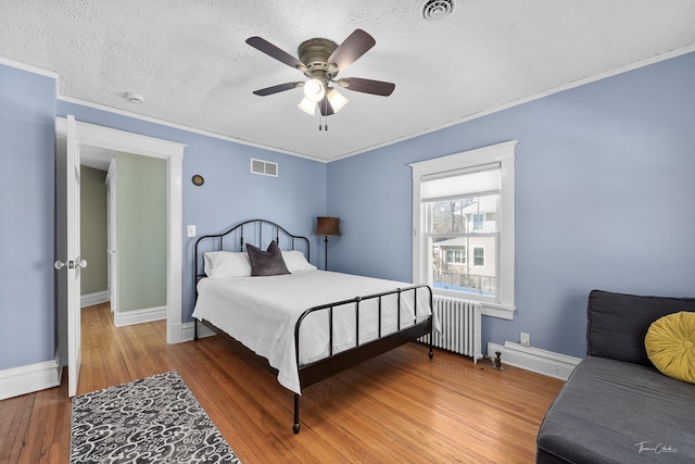 bedroom featuring visible vents, radiator heating unit, ornamental molding, wood finished floors, and a textured ceiling