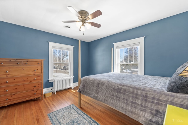 bedroom featuring visible vents, light wood finished floors, radiator heating unit, and multiple windows