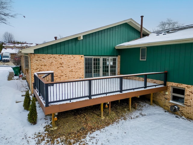 snow covered back of property with a deck and brick siding