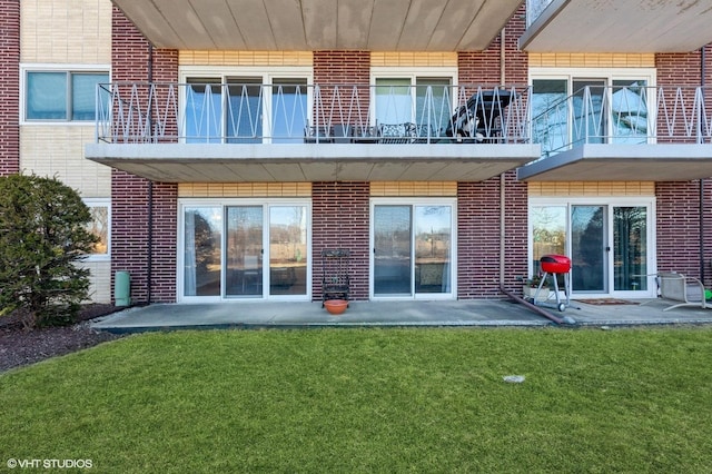 back of house featuring a yard, a patio, brick siding, and a balcony