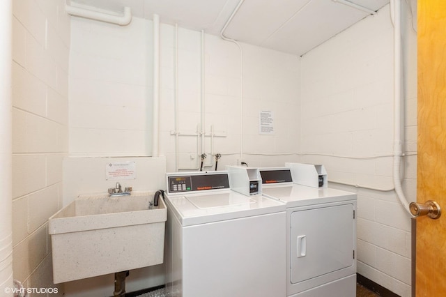 community laundry room with concrete block wall, separate washer and dryer, and a sink