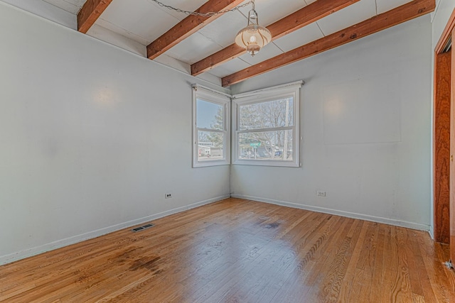 empty room with baseboards, beam ceiling, visible vents, and wood finished floors