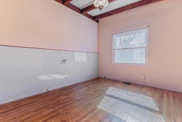 empty room featuring baseboards, beamed ceiling, and wood finished floors