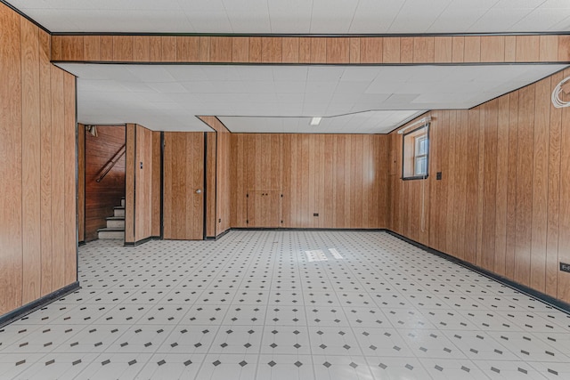 basement featuring stairway, wood walls, and baseboards