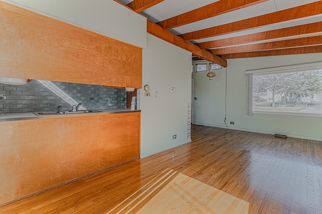 kitchen featuring tasteful backsplash, beamed ceiling, light wood-type flooring, and a sink