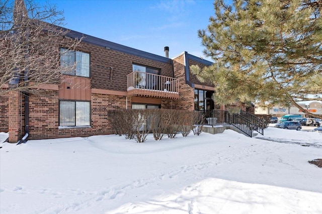 snow covered rear of property with brick siding, mansard roof, and a shingled roof