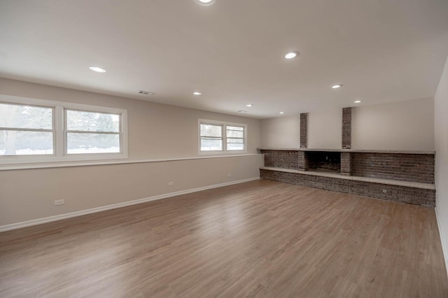 unfurnished living room with visible vents, baseboards, light wood-style flooring, a brick fireplace, and recessed lighting