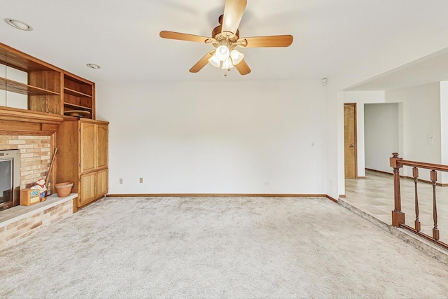 unfurnished living room featuring light carpet, a brick fireplace, baseboards, and a ceiling fan