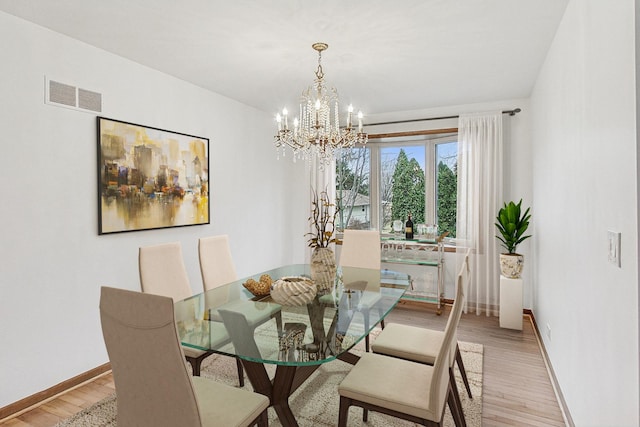 dining area with light wood-type flooring, an inviting chandelier, baseboards, and visible vents