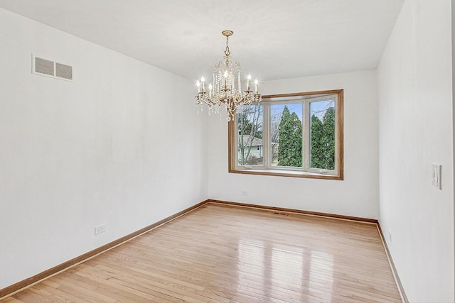 spare room featuring light wood-type flooring, visible vents, baseboards, and an inviting chandelier