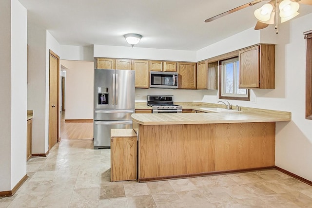 kitchen with baseboards, a peninsula, stainless steel appliances, light countertops, and a sink