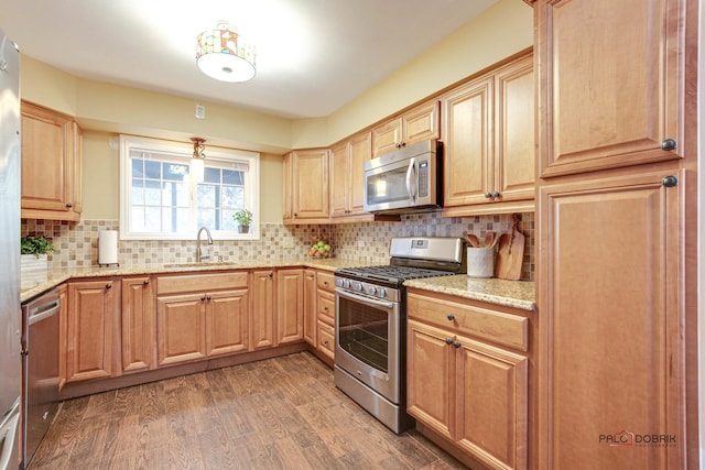 kitchen featuring dark hardwood / wood-style flooring, light stone countertops, sink, backsplash, and appliances with stainless steel finishes