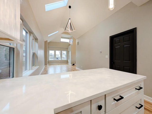 kitchen featuring light hardwood / wood-style flooring, hanging light fixtures, lofted ceiling with skylight, and white cabinets