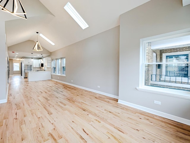 unfurnished living room featuring light wood-type flooring, a skylight, and high vaulted ceiling