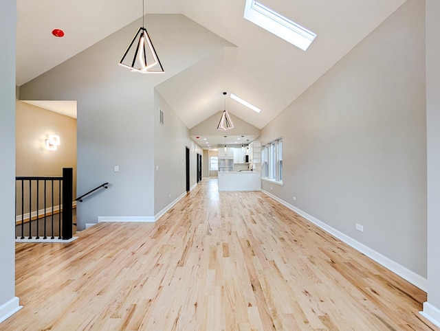 unfurnished living room featuring high vaulted ceiling, light hardwood / wood-style floors, and a skylight