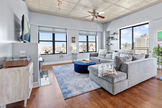 living area with a city view, ceiling fan, baseboards, and wood finished floors