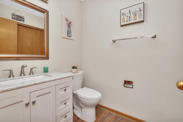 half bath with wood finished floors, vanity, toilet, and baseboards