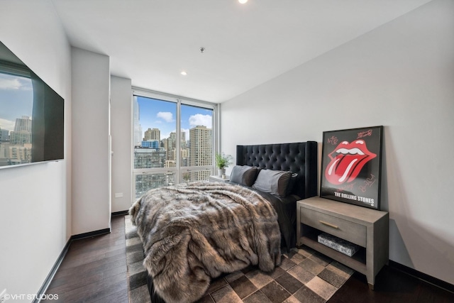 bedroom featuring a view of city, dark wood-type flooring, a wall of windows, and baseboards