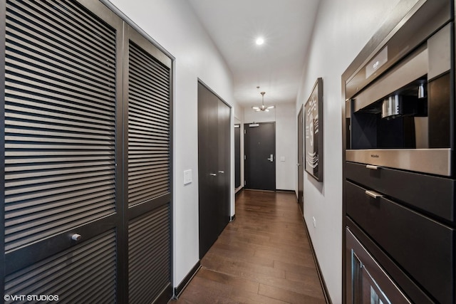 hallway with dark wood-type flooring, recessed lighting, a chandelier, and baseboards