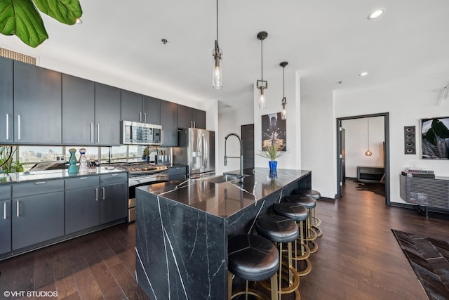 kitchen with a center island with sink, dark countertops, dark wood-style floors, decorative light fixtures, and stainless steel appliances