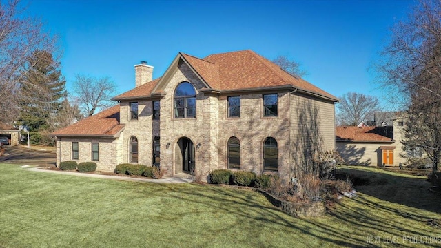 view of front of house featuring roof with shingles, a chimney, a front lawn, and brick siding