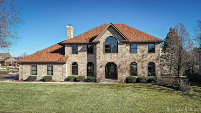 view of front of house featuring brick siding, a chimney, and a front yard