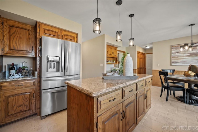 kitchen with light stone counters, a kitchen island, hanging light fixtures, stainless steel fridge with ice dispenser, and brown cabinetry