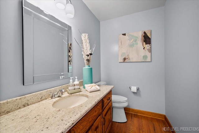 bathroom featuring toilet, baseboards, wood finished floors, and vanity