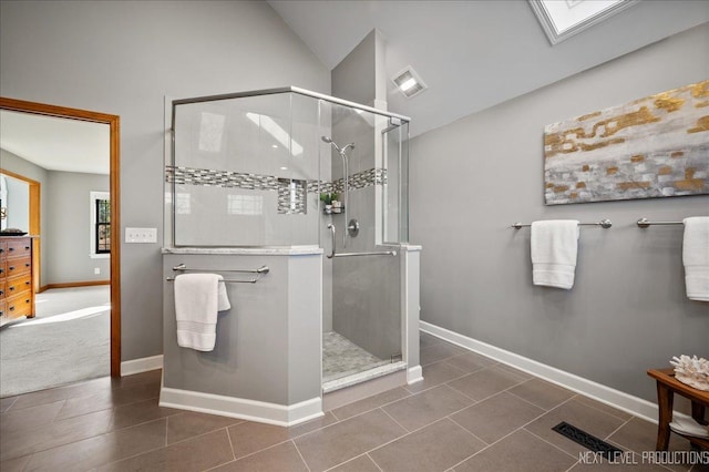 bathroom with a stall shower, visible vents, baseboards, and lofted ceiling with skylight