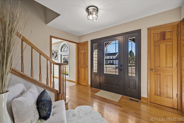 entryway with baseboards, stairs, visible vents, and wood finished floors