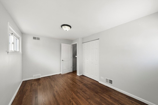 unfurnished bedroom with dark wood-style floors, visible vents, and baseboards